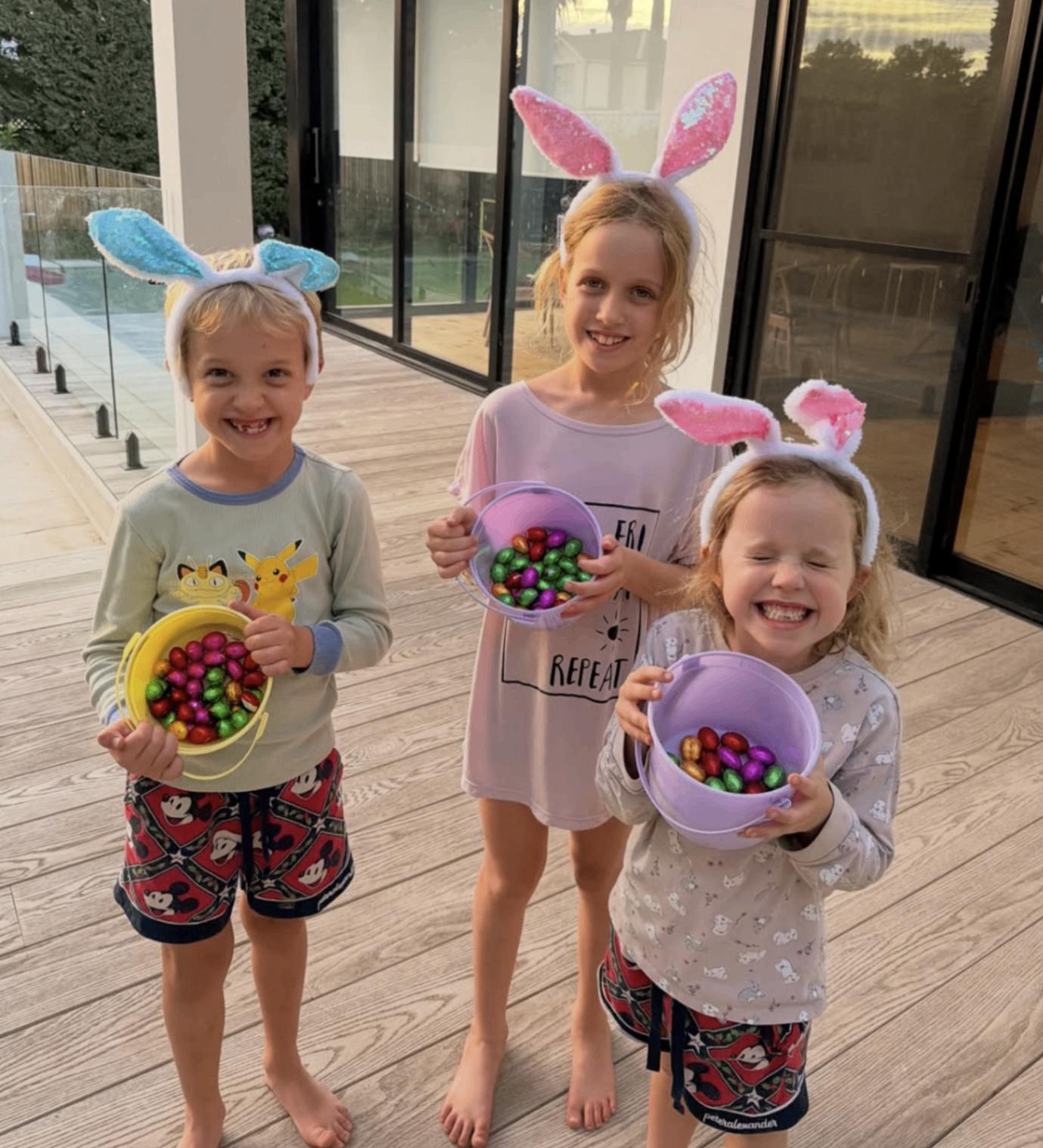 Three children holding buckets of chocolate eggs after an Easter hunt on a home visit in Adelaide